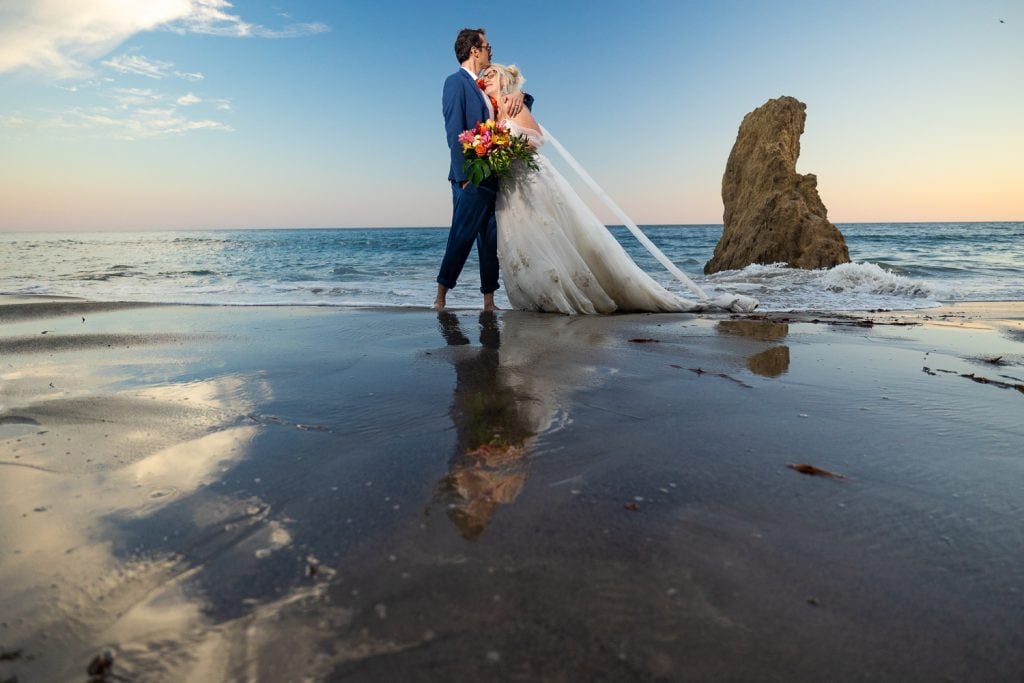 The sunset reflects off the beach as an elopement couple embraces.