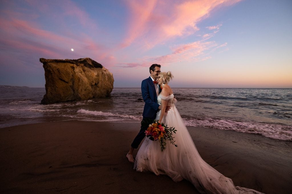A sunset with pink sky over a wedding couple at Malibu Beach.