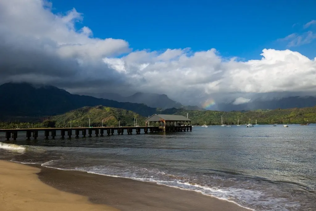 The Hanalei pier in Kauai wit a rainbow over the ocean.