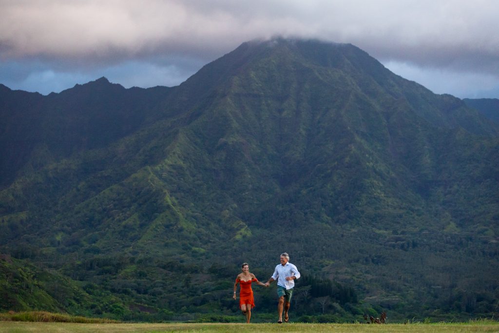 A colorful couple runs toward the photographer with the mountains of Kauai in the background.
