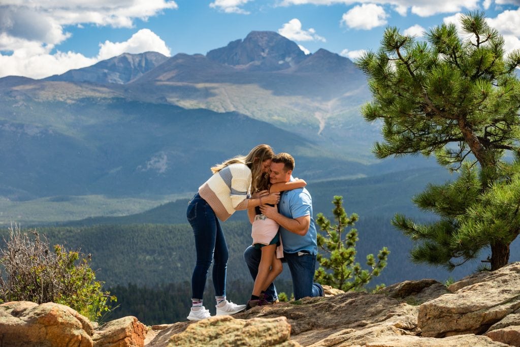 A newly engaged couple hug their daughter in front of a mountain view in Colorado.