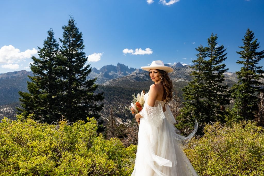A bride wearing a white cowboy hat gives a look over her shoulder.