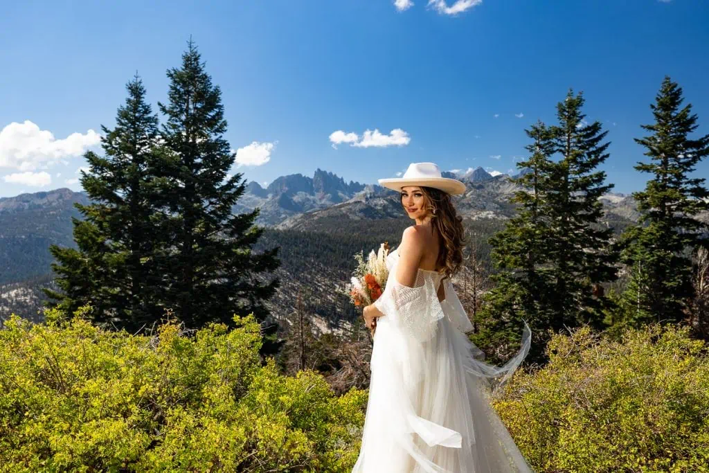 A bride wearing a white cowboy hat gives a look over her shoulder.