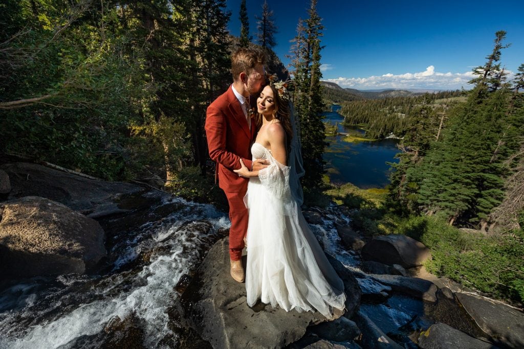 The elopement couple stands in the middle of an epic waterfall.