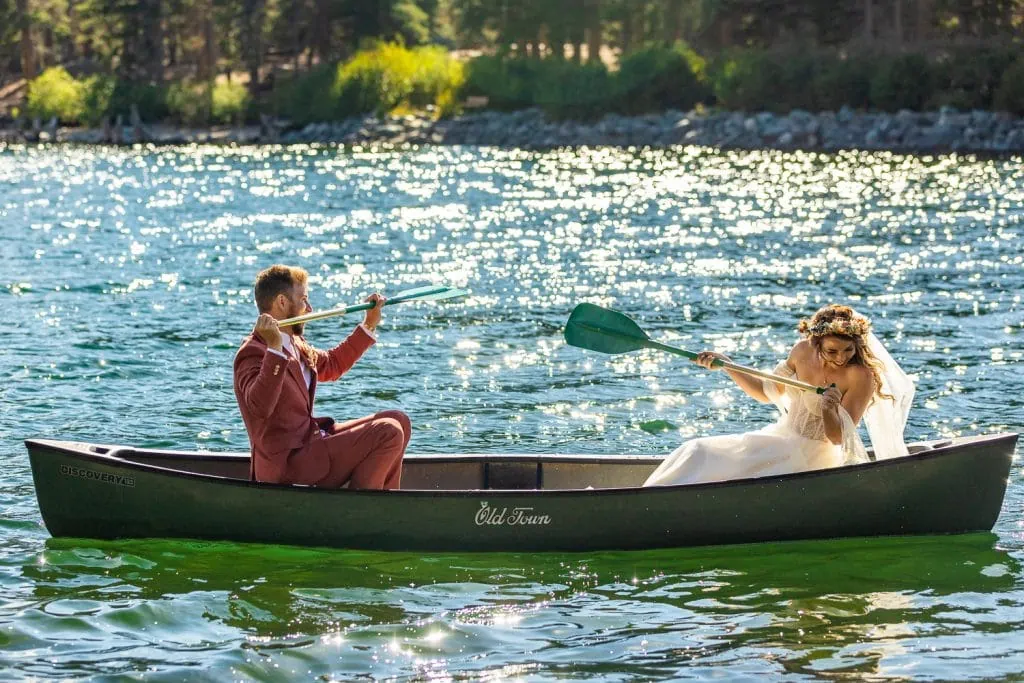 The groom splashes a bride with his canoe paddle on the sparkling lake.