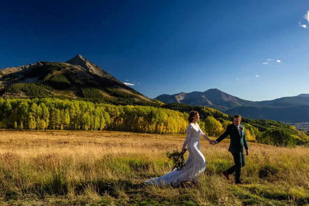 An elopement couple walks through a field of tall grass in Crested Butte, Colorado in fall.