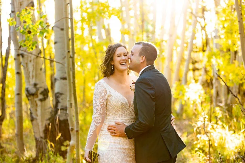 A fall elopement couple giggles together in the golden aspen tree forest.