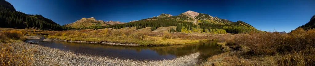 A panoramic image of a calm river in front of a large mountain peak in Crested Butte, Colorado.