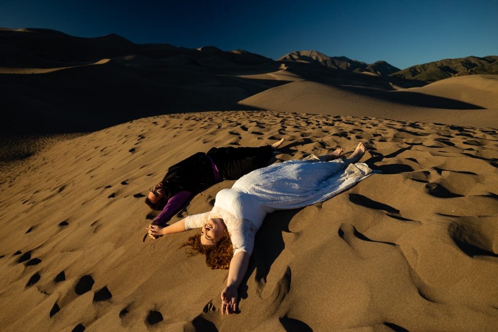 The elopement couple lay on their backs in the sand dunes of Colorado.