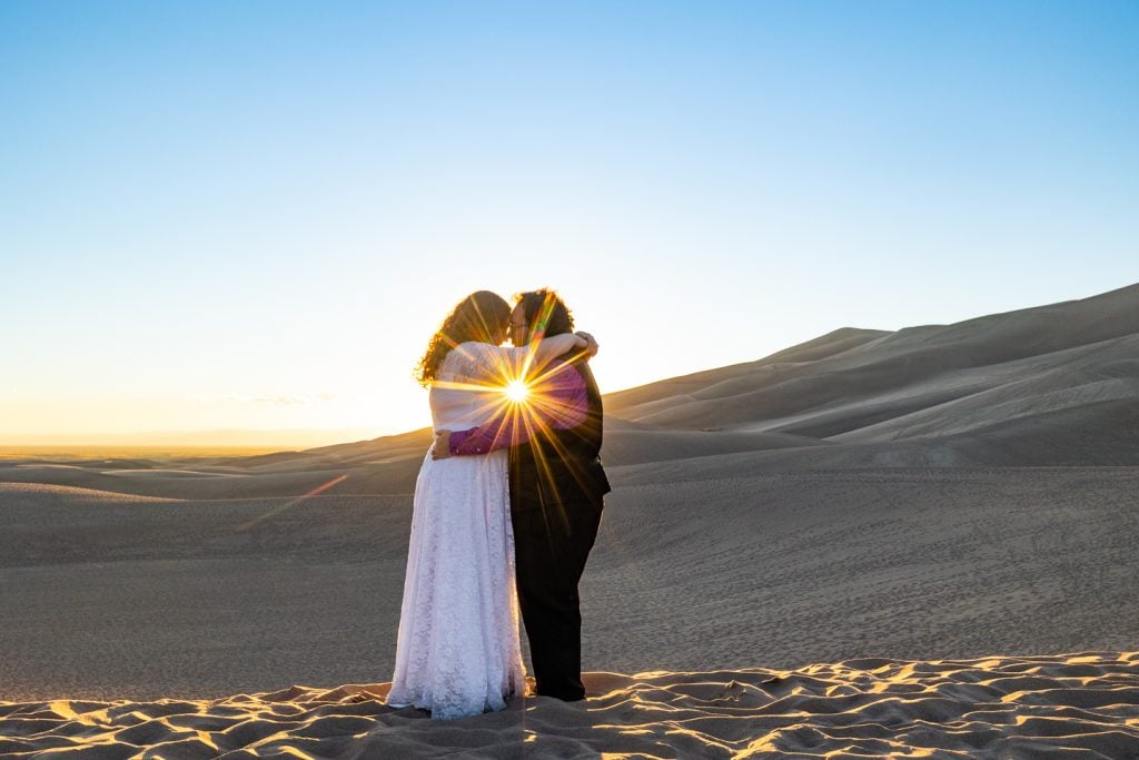 The sun sets behind the elopement bride and groom at Great Sand Dunes national park. 