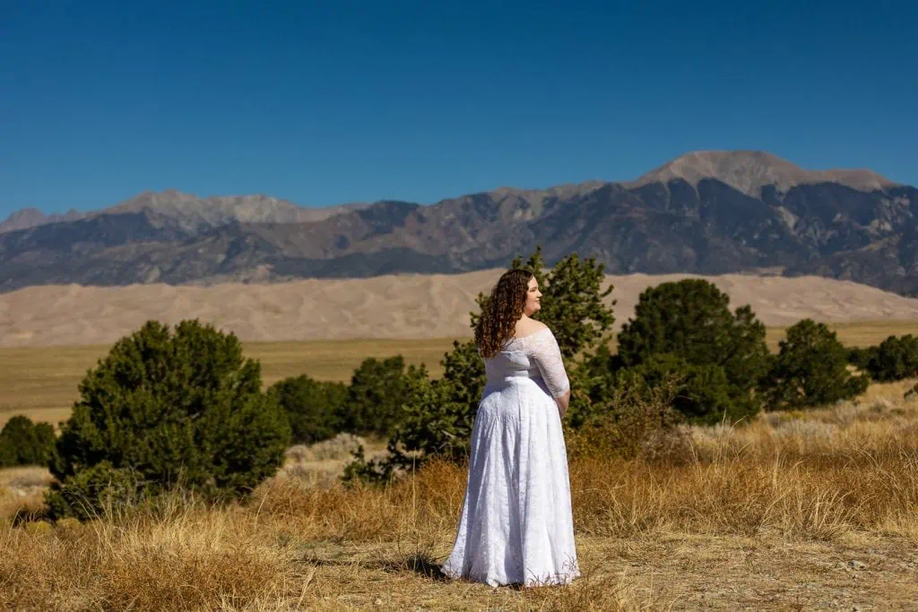 A bride stands in front of the great sand dunes in this colorful photograph.