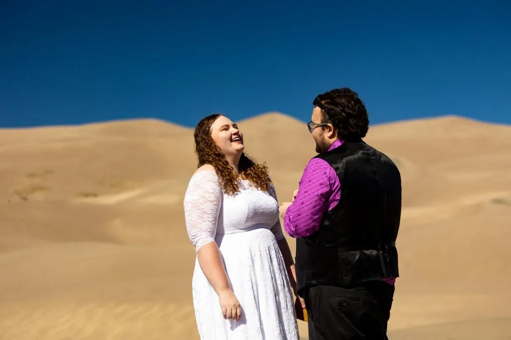 The bride laughs at the groom's vows during their great sand dunes elopement ceremony. 