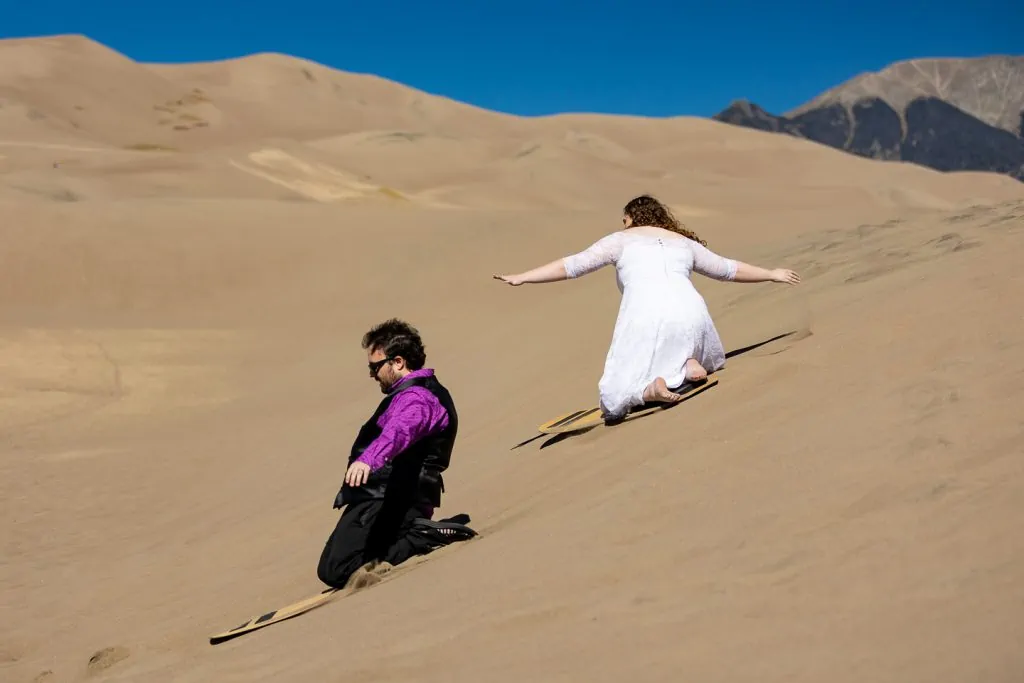 A wedding couple sand sledding at Great Sand Dunes national park in Colorado. 