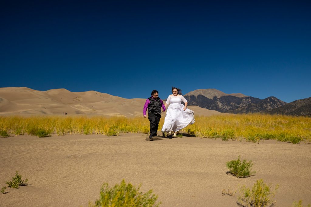 The elopement couple runs across the sand at Great Sand Dunes in Colorado. 