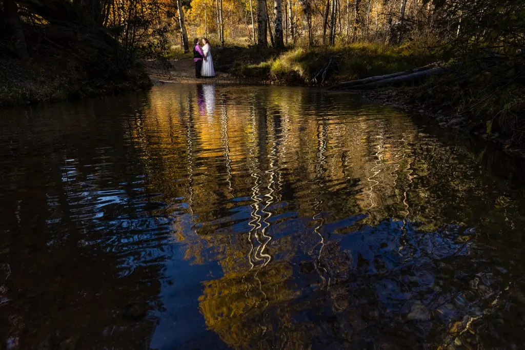 A reflection of a just married bride and groom in the creek with fall colors around them by Great Sand Dunes elopement photographer Lucy Schultz.