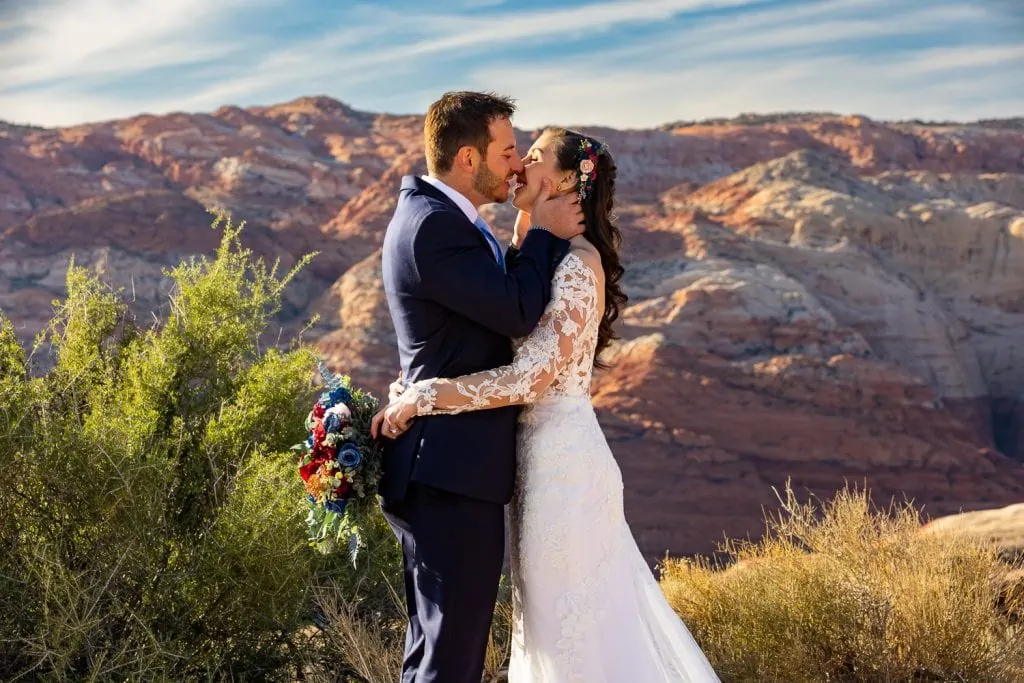 The groom grabs the bride by the face and kisses her in Snow Canyon State Park.