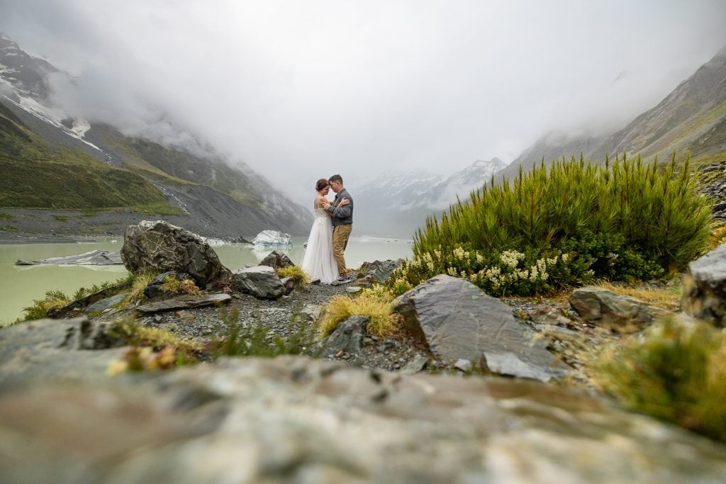 The elopement couple shares their first dance at Mt. Cook on the shore of Hooker Lake, with icebergs floating in the lake behind them. 