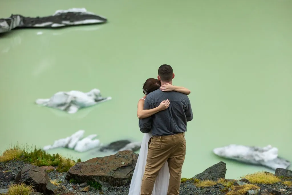 An elopement couple shares their first dance at Hooker lake, where icebergs are floating in the greenish glacial water.