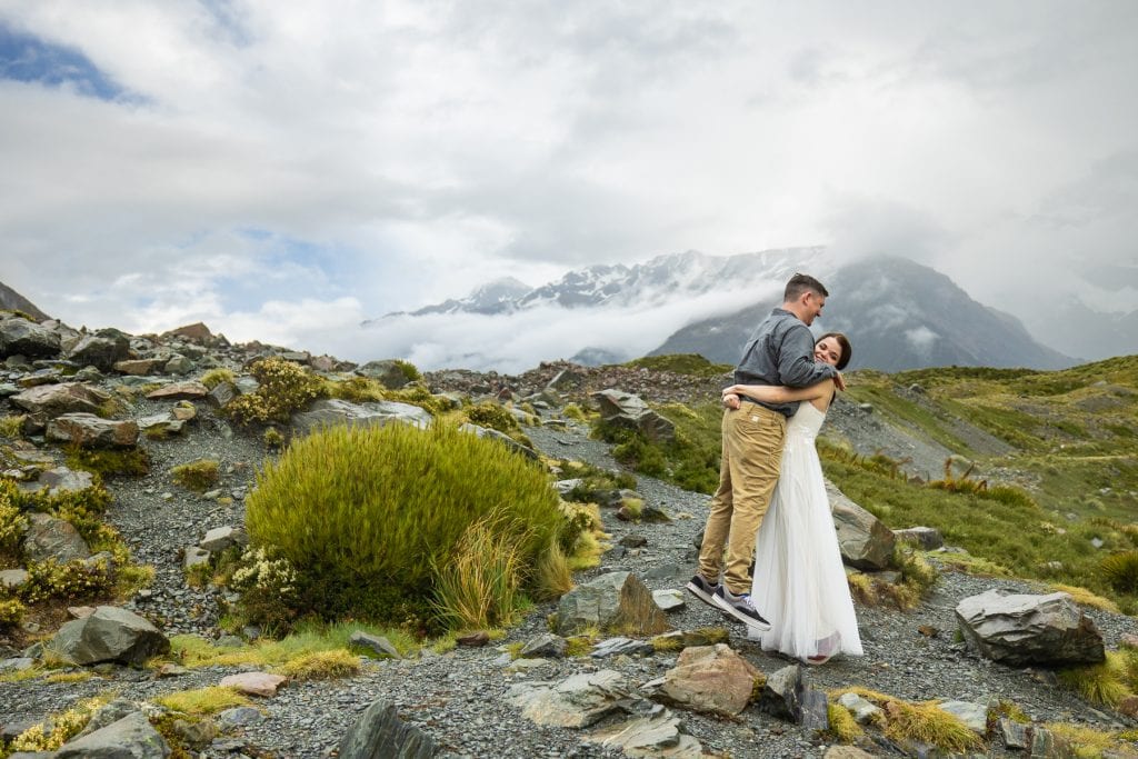 The bride picks up the groom playfully in the green mountain scenery of New Zealand's South Island. 