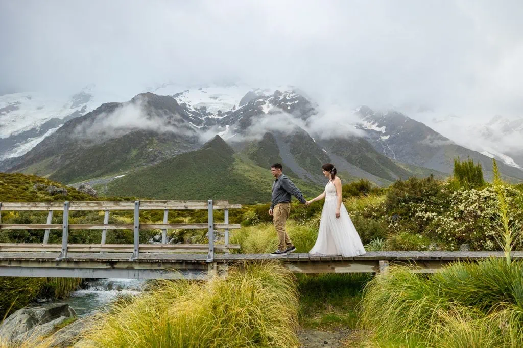 A hiking elopement couple takes on a rustic bridge over a glacial river at Mt. Cook, South Island New Zealand. 