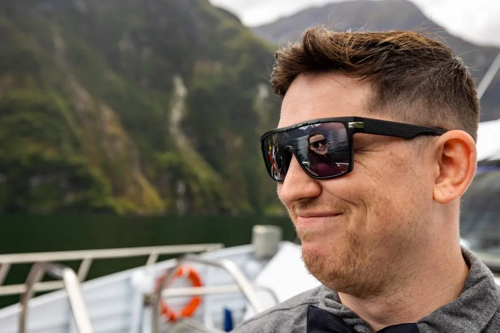 The bride's face is reflected in the groom's sunglasses on a boat ride.