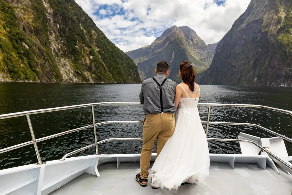 An Adventure elopement couple on a boat cruise on Milford sound with the mountain fjords in the background.
