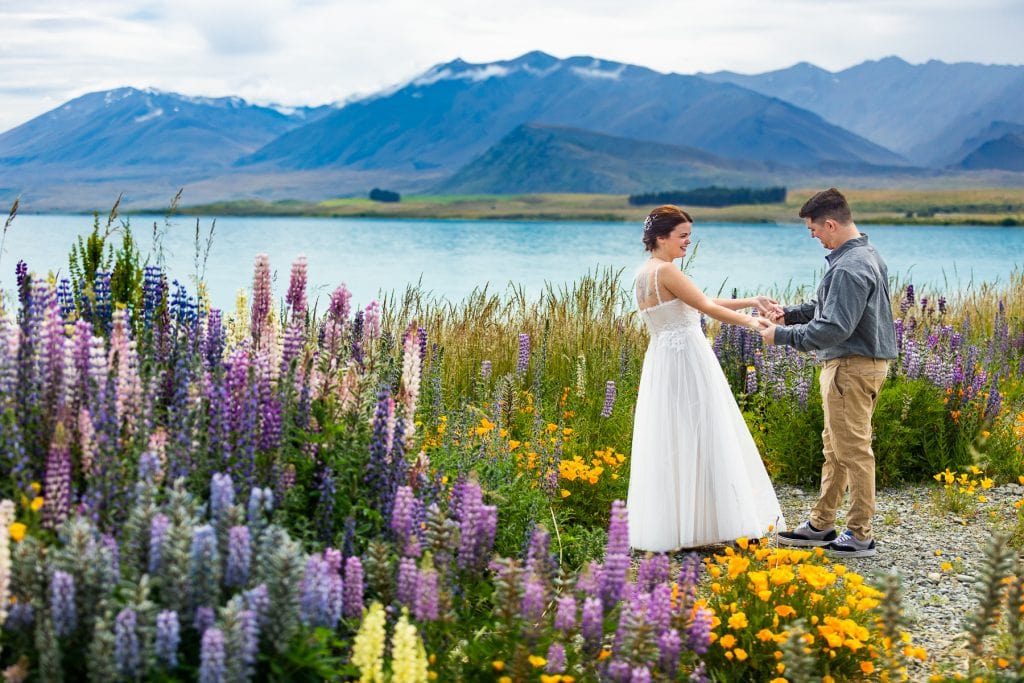 A bride and groom share a first look at lake tekapo, new zealand at their adventure elopement in the purple and blue flowers.
