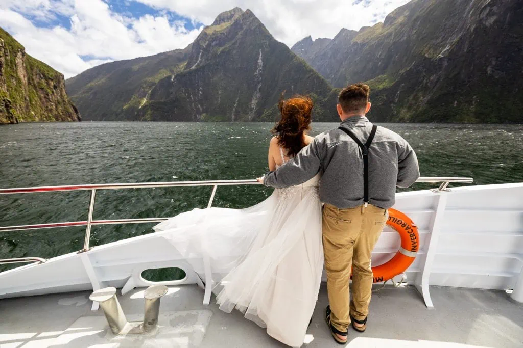 Wind blows the bride's dress on the bow of the boat in Milford Sound in this colorful photo.