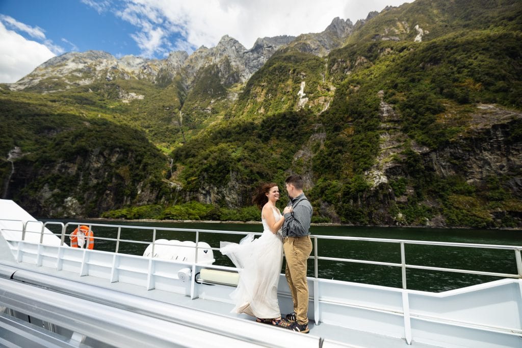 A bride and groom hold each other on a windy boat ride in the fjords of New Zealand's south Island. 
