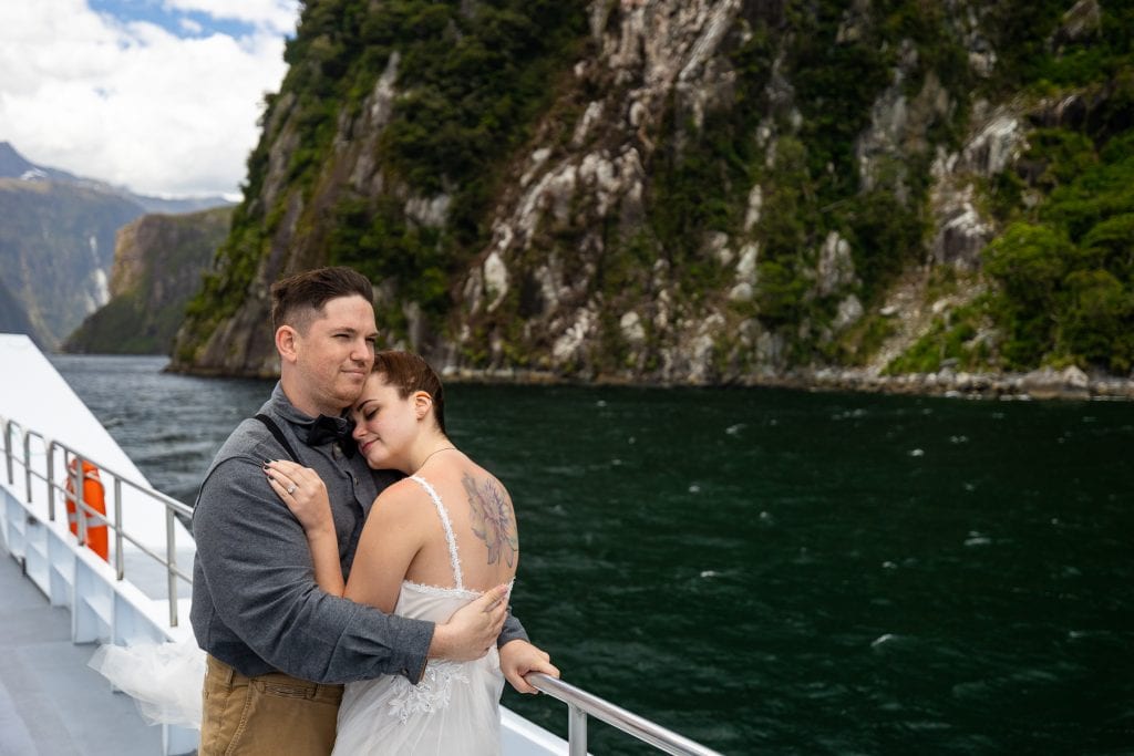 The groom embraces his bride while sightseeing on Milford Sound, New Zealand. 