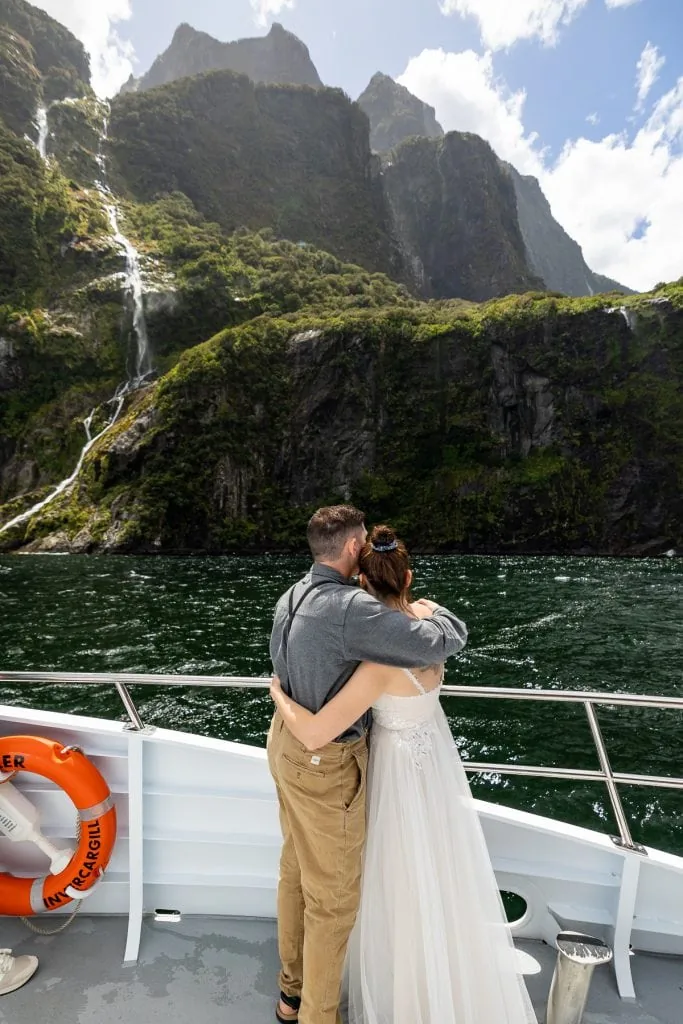 An elopement at Paradise falls in Milford Sound New Zealand. Blue sky is visible over the towering mountains.