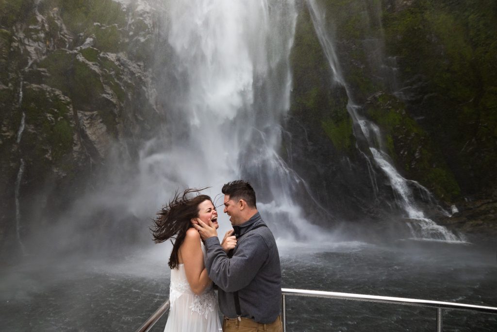 The bride and groom are pummeled by a powerful waterfall during their elopement in New Zealand.