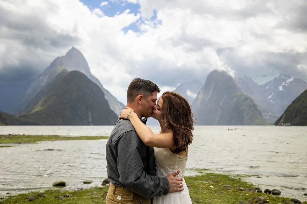 The bride and groom kiss in front of Mitre Peak and the mountains of Milford Sound in Fjordland National Park, South Island New Zealand.