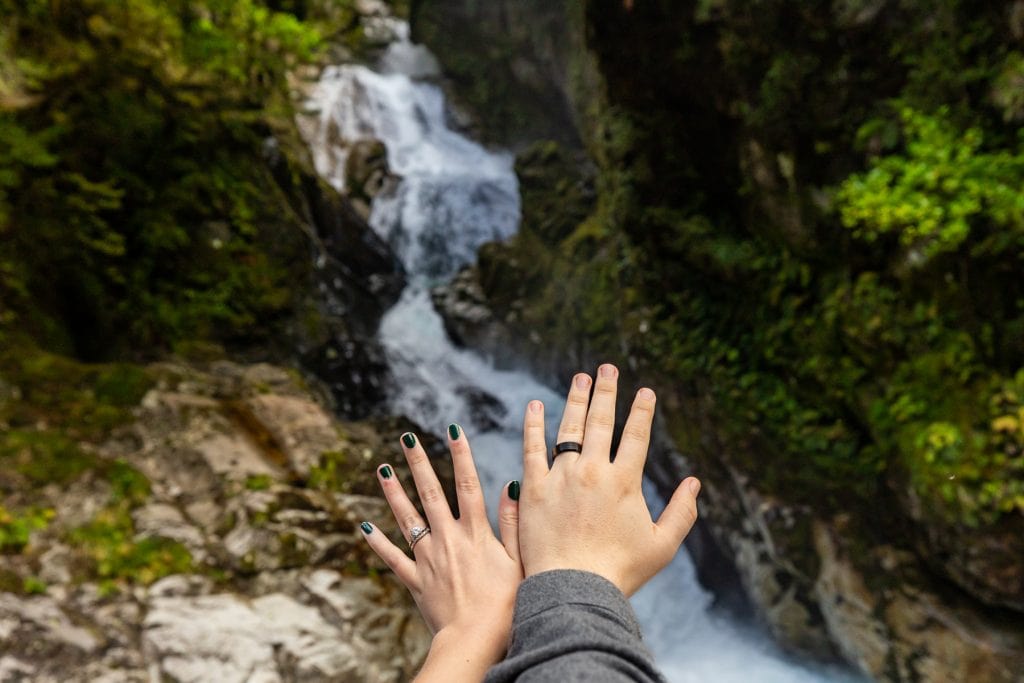 The elopement couple's newly furnished wedding rings in front of Fall Creek Falls in the fjords of New Zealand.
