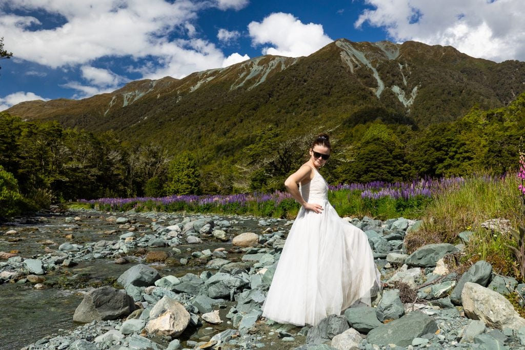 A sassy bride strikes a pose in front of a big mountain range and a field of purple flowers.