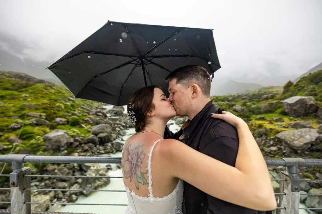 The adventure elopement couple shares a kiss under a black umbrella while it is raining.