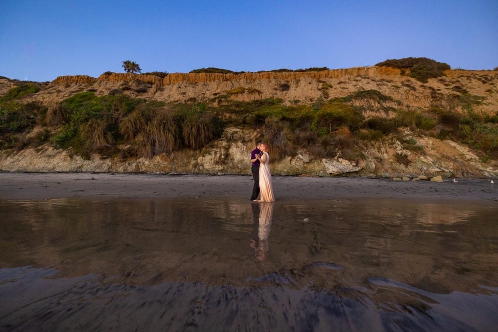 A california elopement location with a could wearing a gold dress and a purple shirt at the ocean.