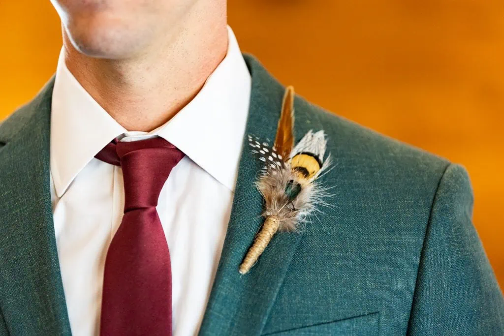 Using crafting and DIY skills, a groom's flower bouttoniere is replaced with feathers to save money.