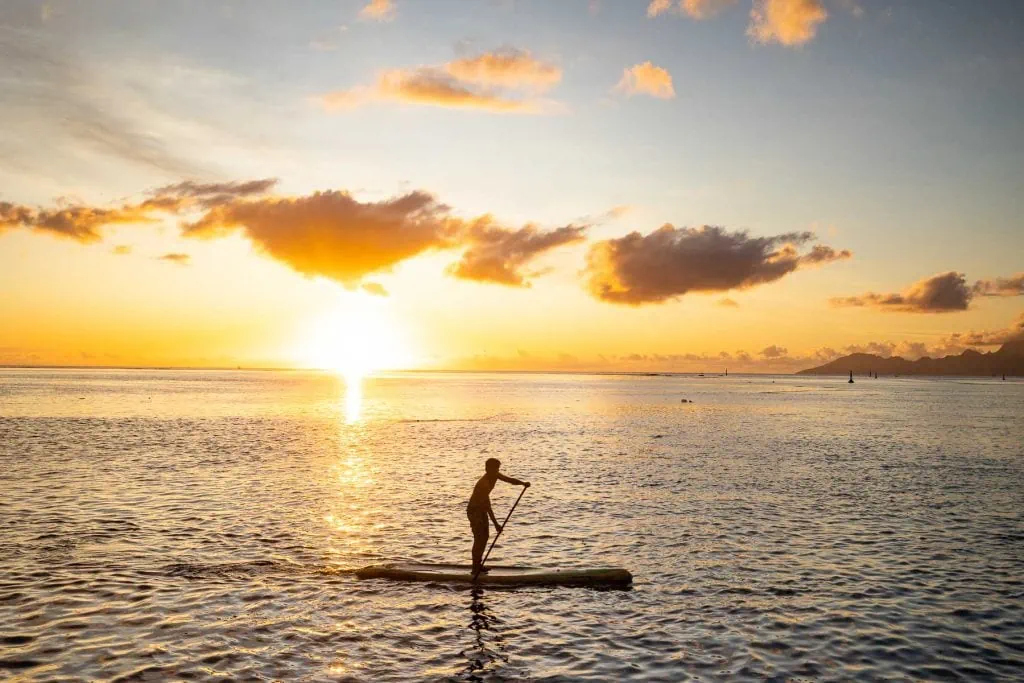 a man on a paddleboard at sunset in Tahiti