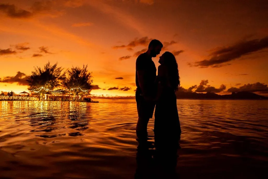 A silhouette of a couple against the orange and yellow sunset of Tahiti by Tahiti elopement photographer Lucy Schultz.