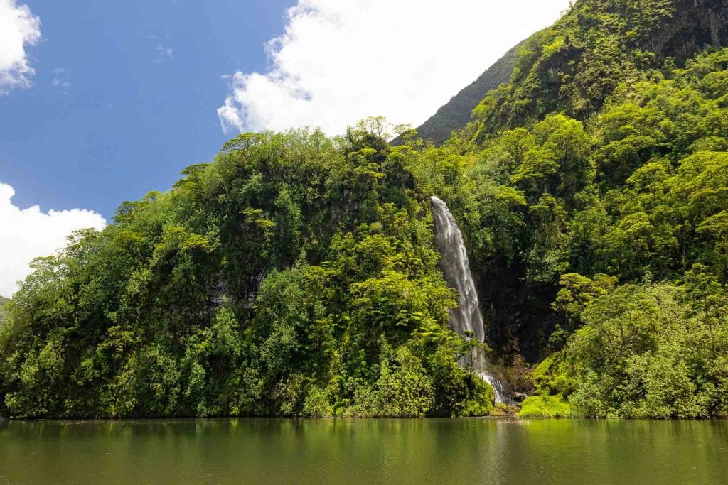 A huge waterfall in Tahiti plunges into a lake that reflects the green jungle around it.