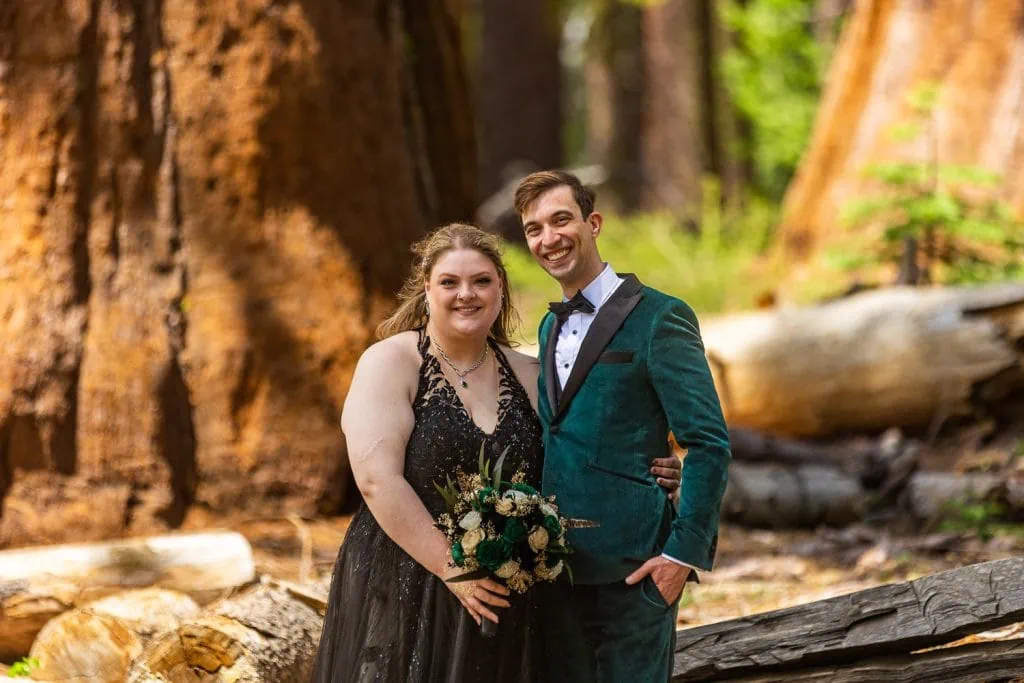 A yosemite elopement portrait of the bride in a black dress and the groom in a green tuxedo smiling at the camera.