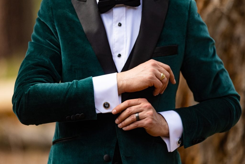 A stylish groom in a green velvet tuxedo shows off his gearstick cufflinks in this detail photo.