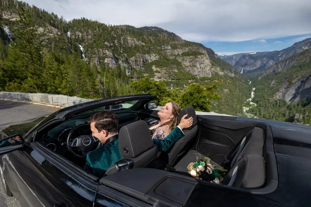 The elopement couple laughs together while overlooking yosemite national park from their black convertible.