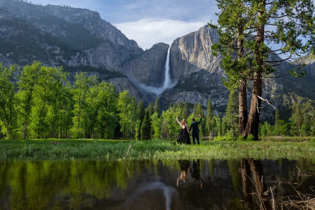 The elopement couple poses for yosemite elopement photos with Yosemite Falls in the background, with the flooded meadow providing a mirrored reflection.