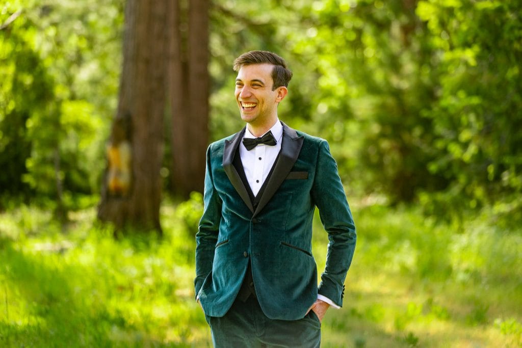 The groom, dressed in a green velvet tuxedo, laughs at something off camera.