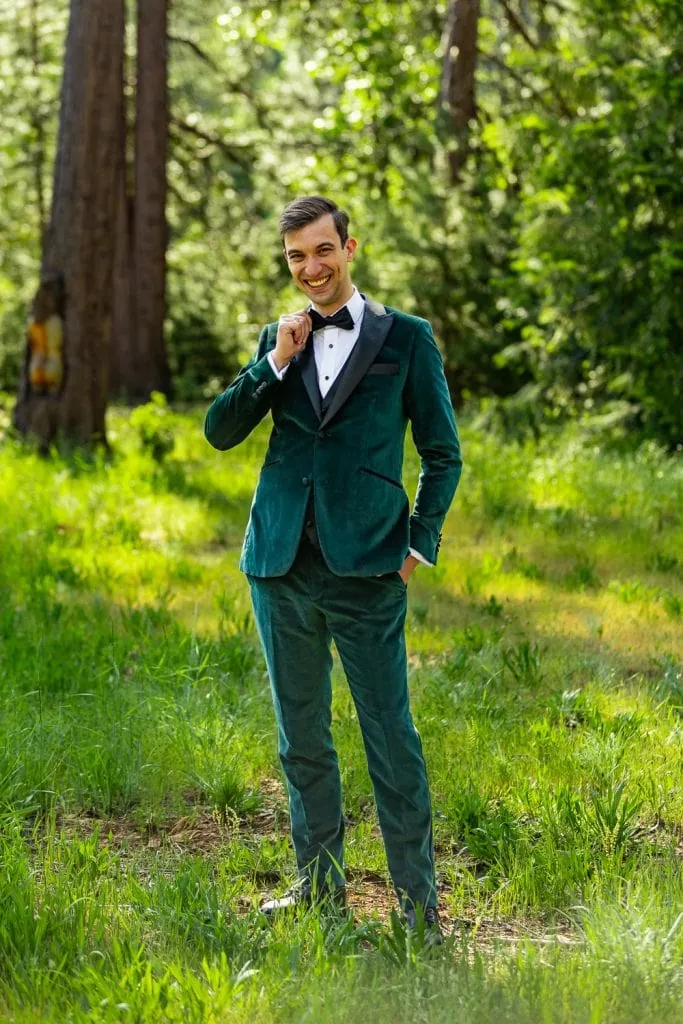 The handsome yosemite groom dressed in a green tuxedo straightens his bow tie.