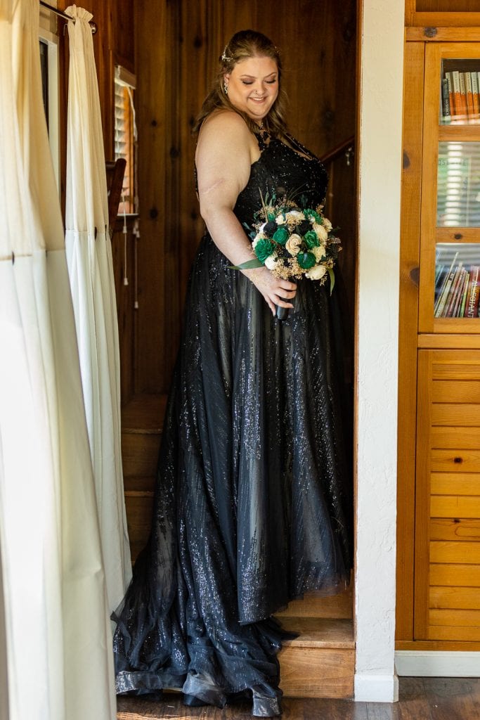 A bride wearing a black gown stands in a cabin doorway.