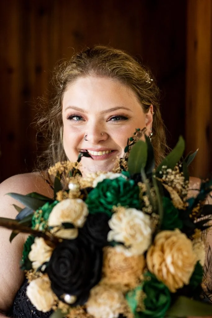 A bridal portrait of an edgy bride looking over the top of her green, white and black flowers.