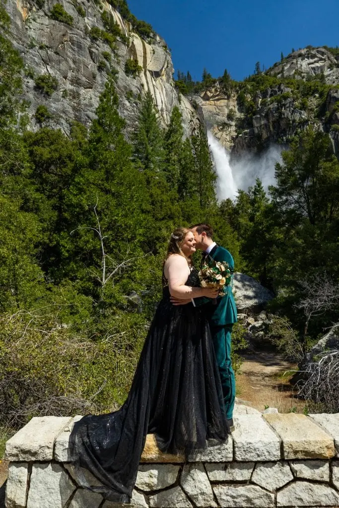 The bride and groom stand in front of cascade falls in Yosemite national park in this elopement photo.